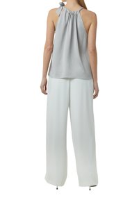 Helles graues Trägershirt mit gerafftem Stoff, das eine fließende Silhouette bietet. Kombiniert mit weiten weißen Hosen und dezenten Hardware-Akzenten.