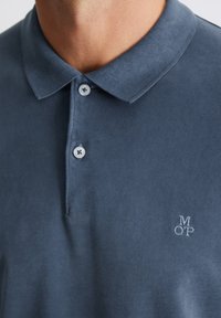 Donkerblauwe polo met een gestructureerde kraag, een placket met twee knopen en geborduurd logo in het wit op de linkerkant van de borst. Zachte stof.