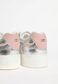 Metallilised hõbedased spordijalatsid roosa sametist kandja aktsentidega, valge kummist tallaga ja tekstuuriga mustriga külgedel. Juhuslik disain ja nöörimisega sulgemine.