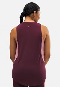 Top atlético sin mangas en color marrón y rosa, con un diseño de cuello redondo y dobladillo curvado. Detalle sutil del logo en la parte posterior. Textura suave.