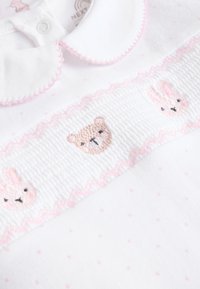 Robe en coton blanc à pois roses, avec un panneau froncé orné de motifs brodés d'ours et de lapin, et un col festonné.