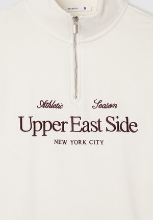 Biała polarowa bluza z krótkim zamkiem na szyi z haftowanym tekstem w ciemnym brązie: "Athletic Season Upper East Side Nowy Jork." Gładka faktura.