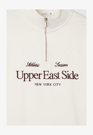 Biała polarowa bluza z krótkim zamkiem na szyi z haftowanym tekstem w ciemnym brązie: "Athletic Season Upper East Side Nowy Jork." Gładka faktura.