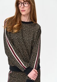 Leoprint sweatshirt met zwarte geribde halslijn en manchetten, met rode en crèmekleurige gestreepte accenten op de mouwen. Zachte textuur.