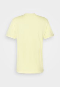 T-shirt uni jaune clair à manches courtes, présenté de dos avec un col rond, sur un fond gris clair.