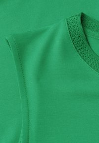 Haut sans manches vert tricoté avec un col en V texturé et un corps en tissu lisse visible en gros plan.