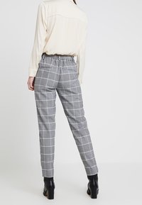 Šedé kostkované kalhoty vyrobené z hladké látky s elastickým pasem. Úzký střih nohavic; nošeny s světle barevnou košili s dlouhým rukávem.