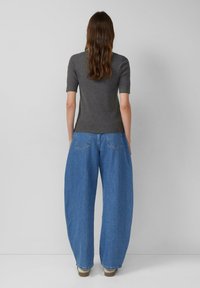 Koolgrijze getailleerde top met korte mouwen, gecombineerd met losvallende blauwe denim jeans. De jeans hebben een traditioneel zakontwerp en wijde pijpen.