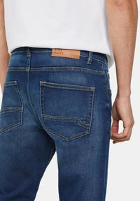 Blue denim jeans with a straight cut, featuring yellow stitching, two back pockets, and a brown leather patch with "BLUE RIDGE" branding.