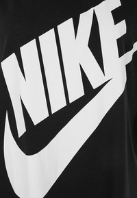 Zwart katoenen t-shirt met een groot wit Nike-logo op de voorkant, met de iconische swoosh geïntegreerd in het ontwerp.