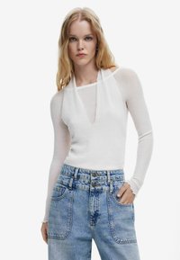 Haut à manches longues blanc avec un décolleté rond, texture douce et design épaules dénudées, associé à un jean en denim bleu clair taille haute.