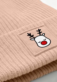 Light pink knitted beanie with a ribbed texture featuring a square patch of a cartoon reindeer face with antlers and a red nose.