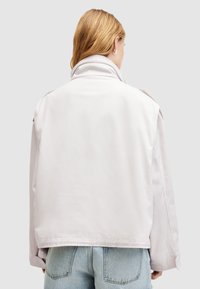 Chaqueta gris claro con un ajuste holgado, que presenta un cuello alto, hombros caídos y un diseño minimalista. Textura suave y sin cierres visibles.