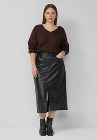 Bordeauxrode gebreide trui met een V-hals, gecombineerd met een zwarte leren midirok met een voorzijde split en zwarte enkellaarzen.