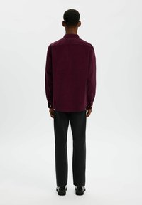 Bordeauxkleurig corduroy overhemd met lange mouwen, knoopmanchetten en kraag; gedragen met zwarte recht-toe recht-aan broek en zwarte schoenen. Achteraanzicht.