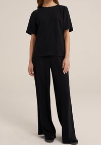 Černý set s krátkým rukávem a širokými kalhotami, vyrobený z měkké tkaniny s hladkou texturou. Rovnbatý střih, uvolněný střih, vhodný pro volnočasové nošení.