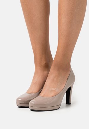 Escarpins en cuir verni beige avec un bout arrondi, une plate-forme proéminente et un talon aiguille noir, mettant en avant une texture lisse et brillante.