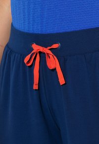 Marineblauwe shorts met een gestructureerde tailleband en een oranje trekkoord met metalen oogjes voor verstelbaarheid. Zacht, lichtgewicht materiaal.