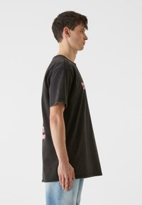 Siva prevelika majica s kratkimi rokavi in zaobljenim ovratnikom, ki vsebuje roza besedilo. Narejena iz mehke bombažne tkanine z rahlo obrabljeno teksturo.