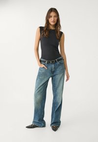 Black sleeveless bodysuit paired with light-wash wide-leg jeans, accentuated by a black belt, and pointed-toe studded black heels.