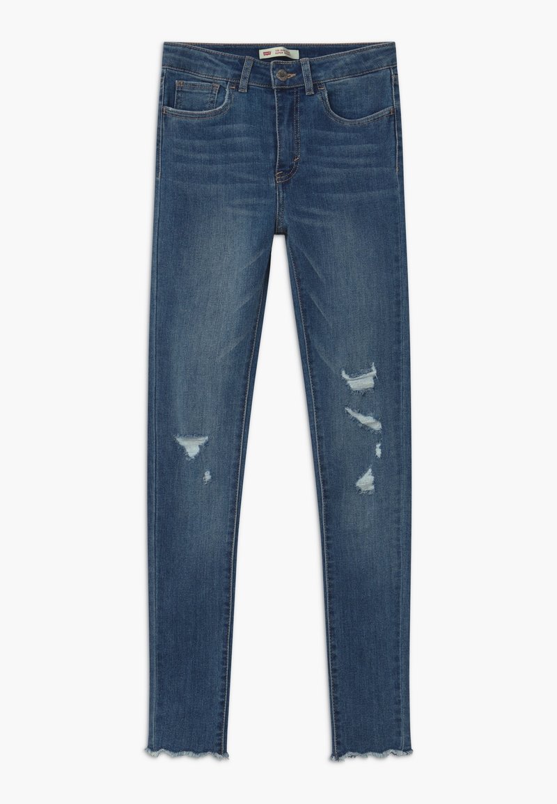 Jean skinny bleu usé avec des ourlets effilochés et cinq poches, présentant un léger effet de décoloration et des détails déchirés sur les deux jambes.
