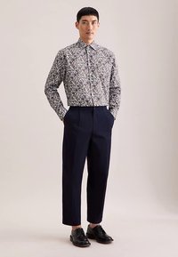 Camicia con bottoni a pressione con motivo floreale in colori tenui, abbinata a pantaloni plissettati blu navy e scarpe eleganti nere. Tessuto dalla texture liscia.