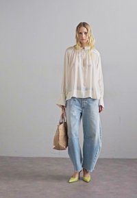 Blusa leggera e trasparente di colore crema con maniche a campana, abbinata a jeans larghi e sbiaditi di color blu. Accessoriata con una borsa beige e tacchi giallo brillante.
