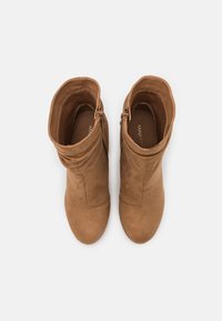 Bottes chevilles en daim marron avec bout arrondi, fermetures éclair latérales et design doux et décontracté. L'intérieur révèle un détail de semelle intérieure de marque.