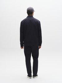 Námořnická bunda a kalhoty z hladké tkaniny, doplněné šedou čepicí a černými botami, zobrazeny zezadu na bílém pozadí.