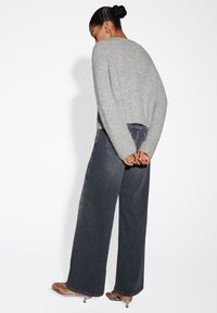 Maglione grigio lavorato a maglia con testo a coste, abbinato a jeans scuri a vestibilità ampia e sandali metallici. Il maglione ha maniche larghe e lunghezza corta.