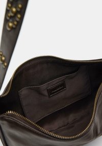 Interno di una borsa in pelle marrone con chiusura a zip, caratterizzato da una superficie liscia, una fodera in tessuto scuro e una piccola etichetta cucita all'interno.