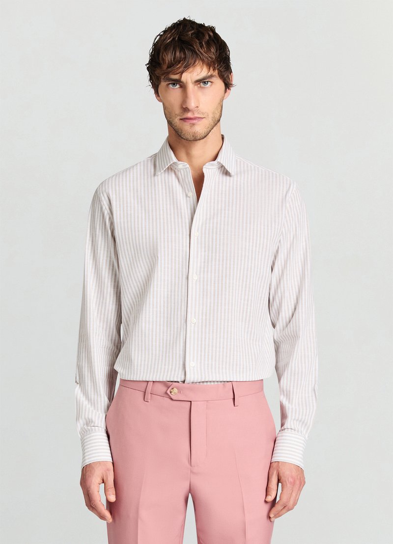 Camicia a righe chiare in bianco e rosa pallido, abbottonata con colletto. Maniche lunghe, tessuto morbido, abbinata a pantaloni da donna rosa con un bottone dorato.