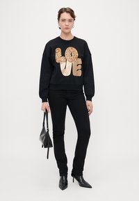 Μαύρο φούτερ με μεγάλο χρυσό γκλίτερ γράμμα "ΑΓΑΠΗ", συνδυασμένο με μαύρα τζιν και μποτάκια. Μια μικρή μαύρη τσάντα ολοκληρώνει το ντύσιμο.