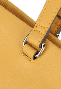 Dettaglio di una borsa a tracolla gialla in pelle con superficie testurizzata, accessori metallici e cuciture a contrasto sulle tracolle.