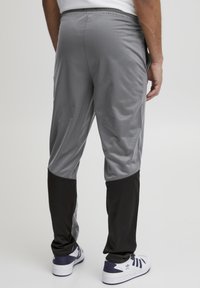 Pantalones deportivos grises con secciones inferiores negras, fabricados en un tejido ligero y suave. Cuentan con una cinturilla elástica y bolsillos laterales.