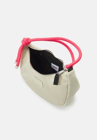 Beige handled pouch med svart dragkedja, ljusrosa flätat handtag och svart inre etikett märkt "Tommy Jeans."