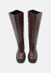 Καφέ δερμάτινες μπότες μέχρι το γόνατο με τετράγωνη μύτη και ελαφριά σόλα με τακούνι. Ο σχεδιασμός έχει ομαλή υφή και φερμουάρ στην εσωτερική πλευρά.