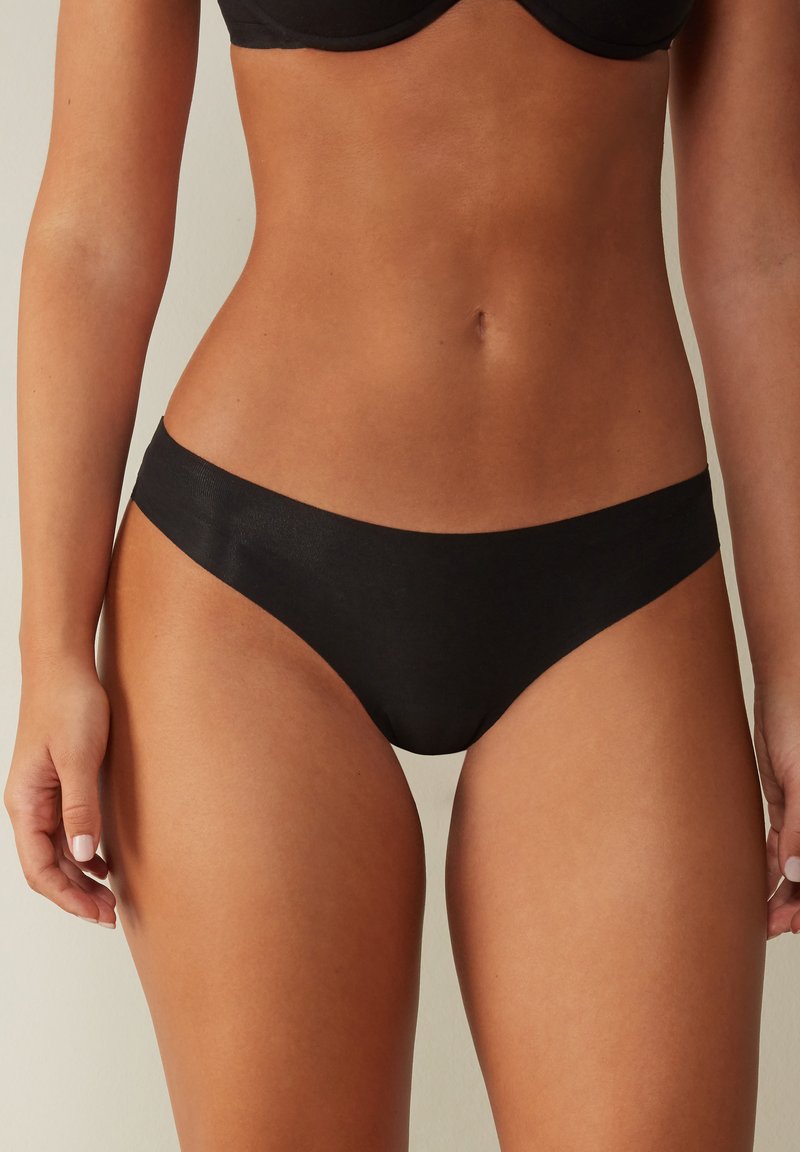 Zwarte bikinibroek met een gladde textuur, een lage taille en minimale bedekking. Beschikt over een naadloze tailleband voor comfort.