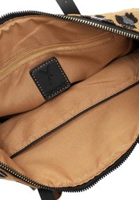 Beige interieur van een tas met een getextureerde zwarte leren label, ritsclosure en een gladde voering met een extra ritsvak.