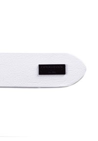 Sangle en cuir blanc avec une étiquette rectangulaire en métal noir embossée avec "Pipobax" et "Est. 1956", présentant une surface texturée et des extrémités arrondies.