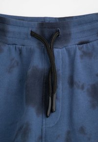 Granatowe spodnie dresowe o miękkiej fakturze, z czarnym sznurkiem, żeberkowym paskiem w talii i subtelnym wzorem tie-dye.