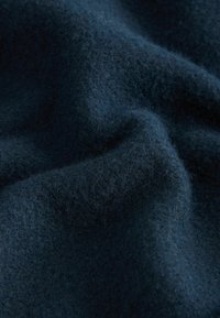 Ciemnoniebieska wełniana tkanina o miękkiej fakturze, z lekko puszystą powierzchnią i delikatnymi fałdami, podkreślająca jej ciepło i głębię.