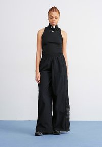 Μαύρο αμάνικο σώμα με ψηλό γιακά και λευκές ρίγες, συνδυασμένο με φαρδιά μαύρα παντελόνια. Λείος υφή, μίνιμαλ αθλητικός σχεδιασμός.