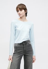 Ανοιχτό μπλε μακρυμάνικη μπλούζα από απαλό, λείο ύφασμα σε συνδυασμό με σκούρο γκρι τζιν παντελόνι ψηλής μέσης· λιτός σχεδιασμός, χωρίς ορατά μοτίβα.