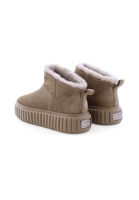 Bottines en suède tan avec doublure en fourrure blanche, semelle épaisse à côtes et couture décorative. L'arrière présente une petite languette de traction et des accents de logo.
