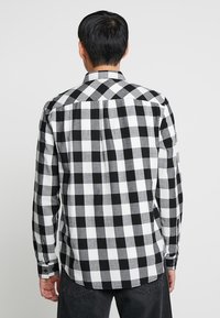 Camicia in flanella a scacchi bianco e nero con maniche lunghe, polsini con bottone e colletto classico. Presenta un yoke e una piega sul retro per un migliore fitting.