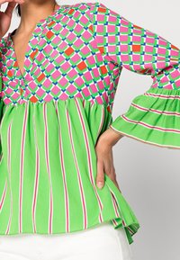 Haut multicolore avec un motif géométrique en rose, vert et rouge sur le buste, accompagné d'un bas évasé à rayures vertes et de manches.