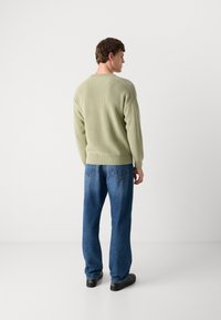 Un pull en tricot vert clair avec un col rond, assorti à un jean en denim bleu ample et des chaussures noires. Vu de dos.