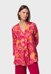 Blusa floral en rosa con patrones botánicos en naranja y amarillo. Presenta un escote en V y mangas largas, fabricada en un tejido ligero.