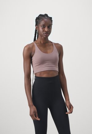 Brun cropped sport bh med spaghetti stropper parret med højtaljede sorte leggings. Glat tekstur, minimalistisk design og tætsiddende pasform.